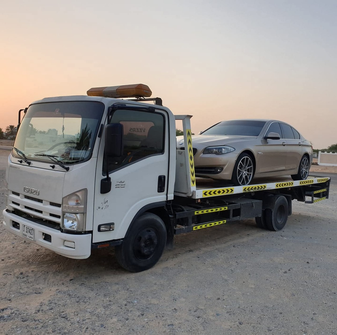 BMW 5 Series recovery on Isuzu flatbed truck at sunset in Dubai outskirts